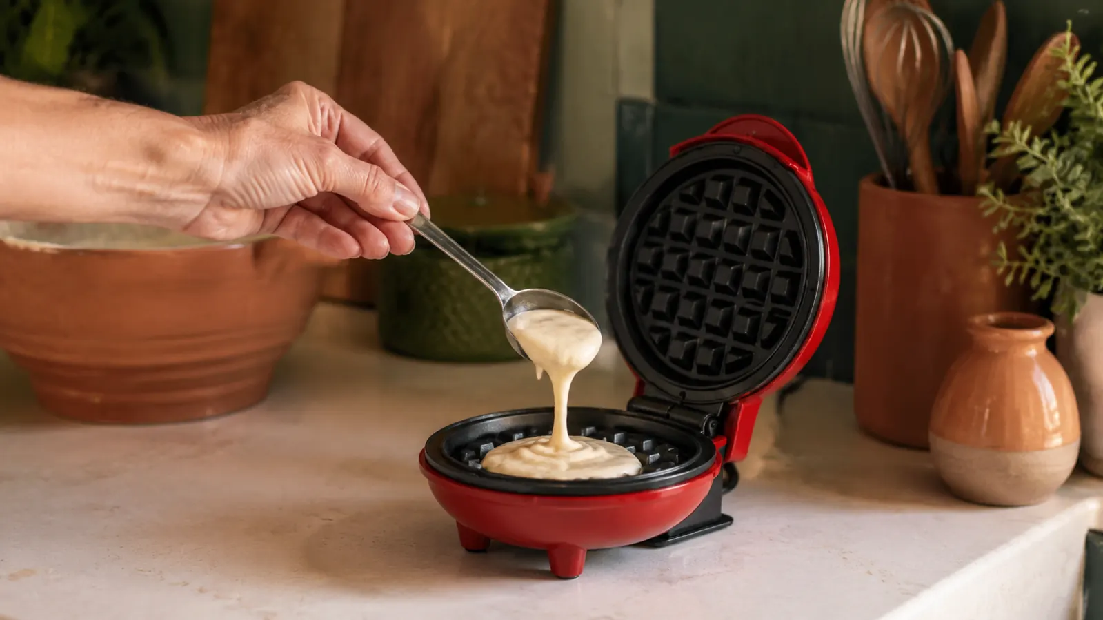 Hand pouring a small amount of waffle batter into the Dash Mini Waffle Maker