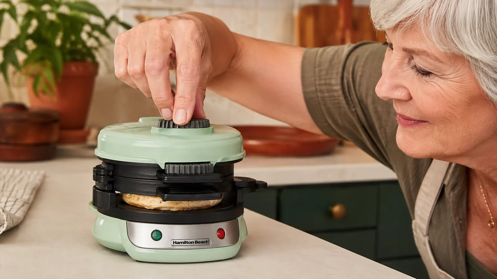 A hand twisting the top plate of the Hamilton Beach Breakfast Sandwich Maker partway through the cook cycle, steam faintly visible